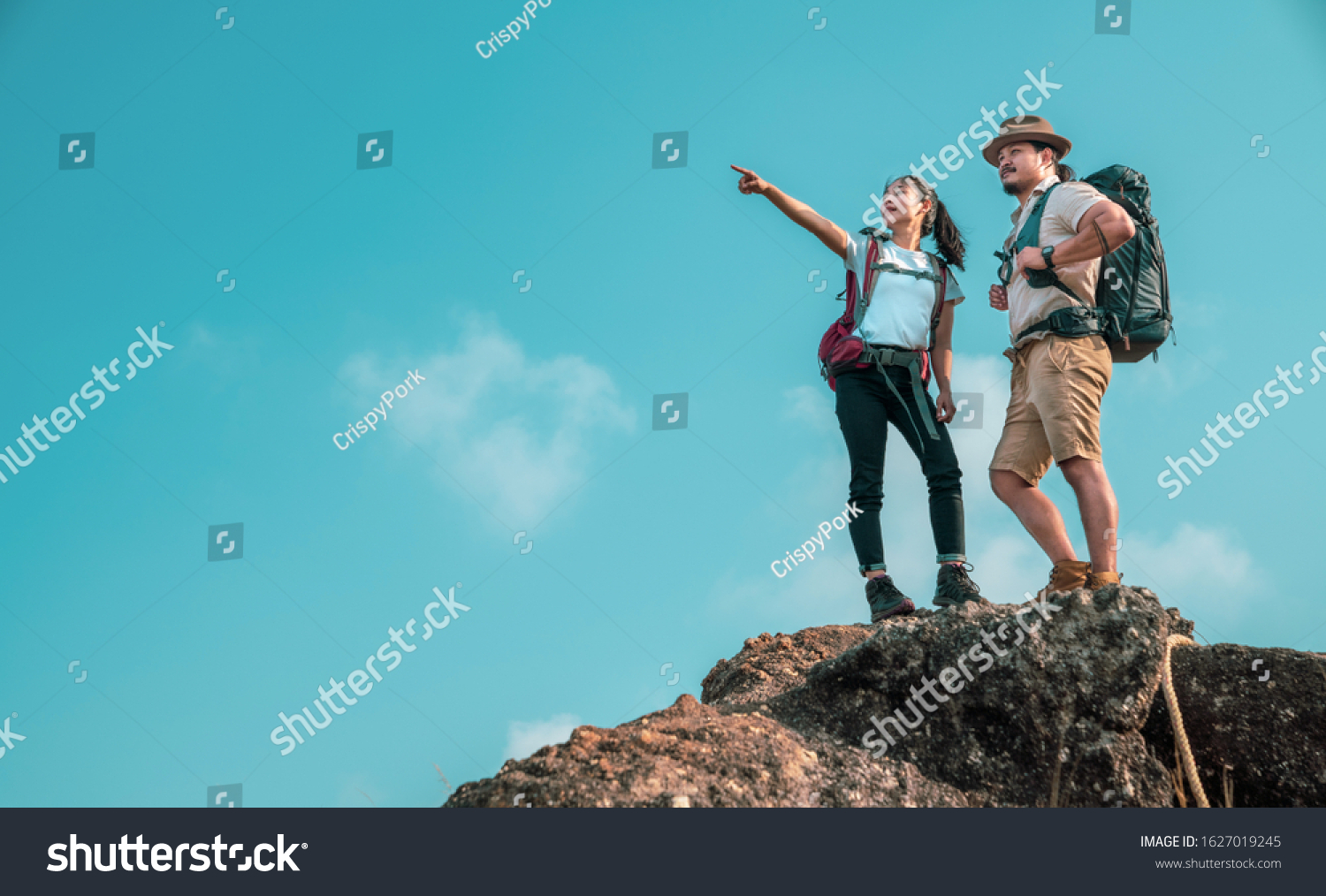 Young asian couple hikers climbing up on the peak of mountain. Two people hikers on top of the mountain enjoying valley view. Tourists with backpacks. Climbing Helps and team work concept