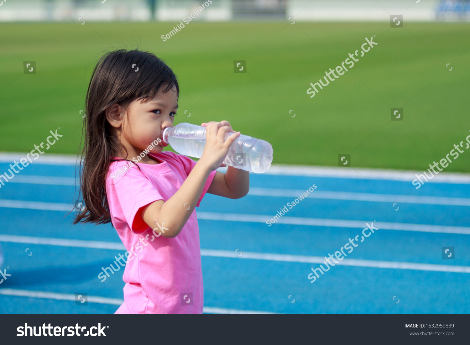 Beautiful Thai girl cute long hair wearing a bitter dress shirt Drinking water from a bottle with thirst Holding two bottles of water to drink After tired from running and playing in the stadium