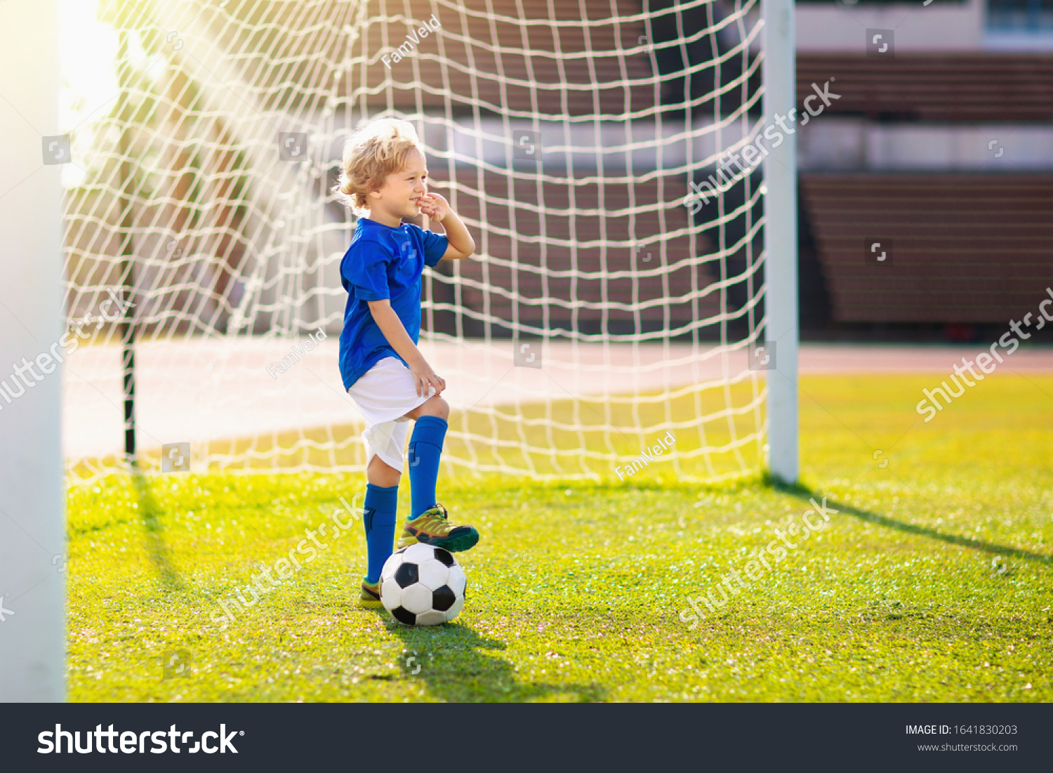 Kids play football on outdoor stadium field. Children score a goal