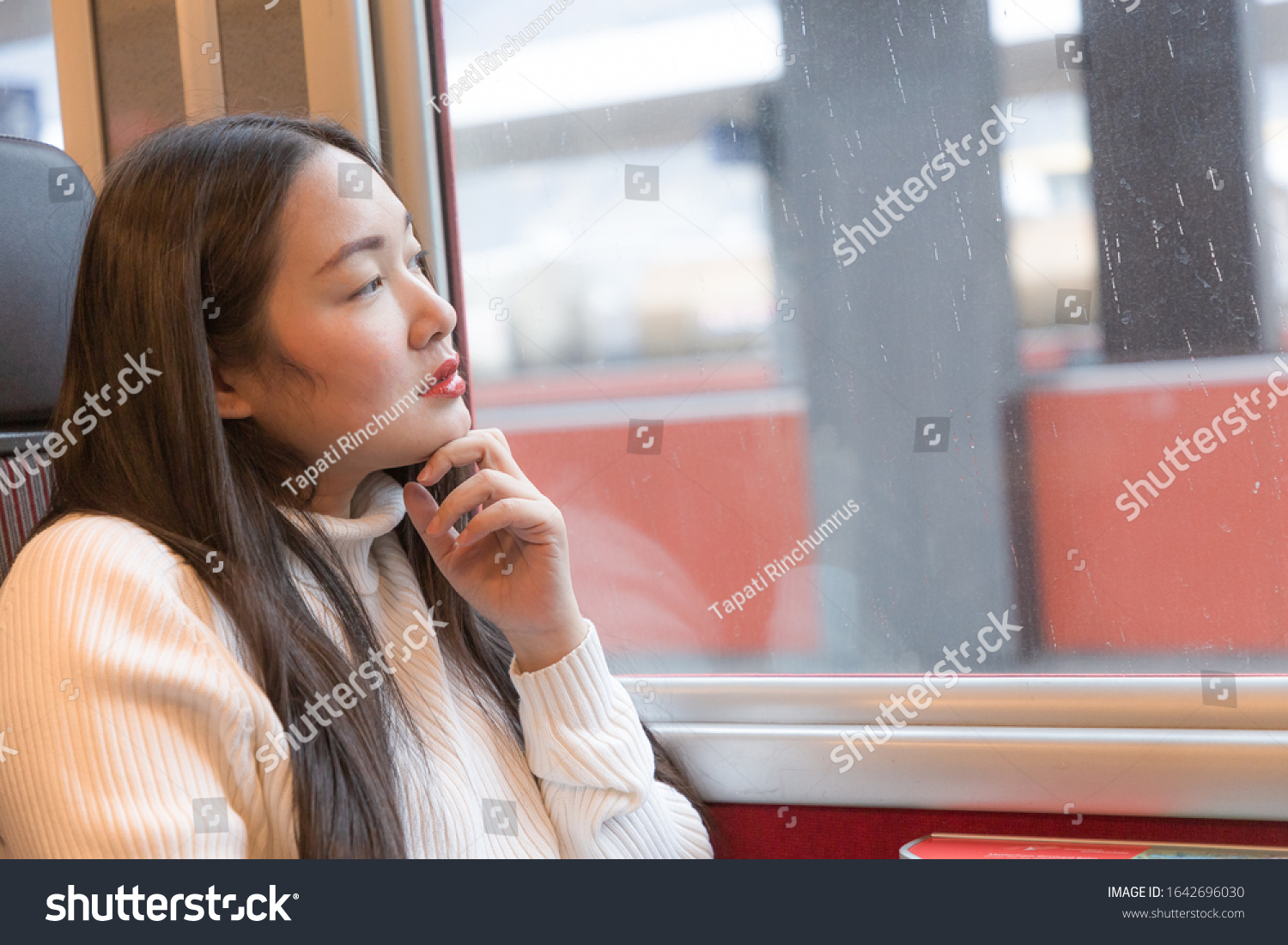 An Asian woman is sitting happily looking at the natural view from the window on the train and traveling on a vacation in Switzerland and planning a train trip.