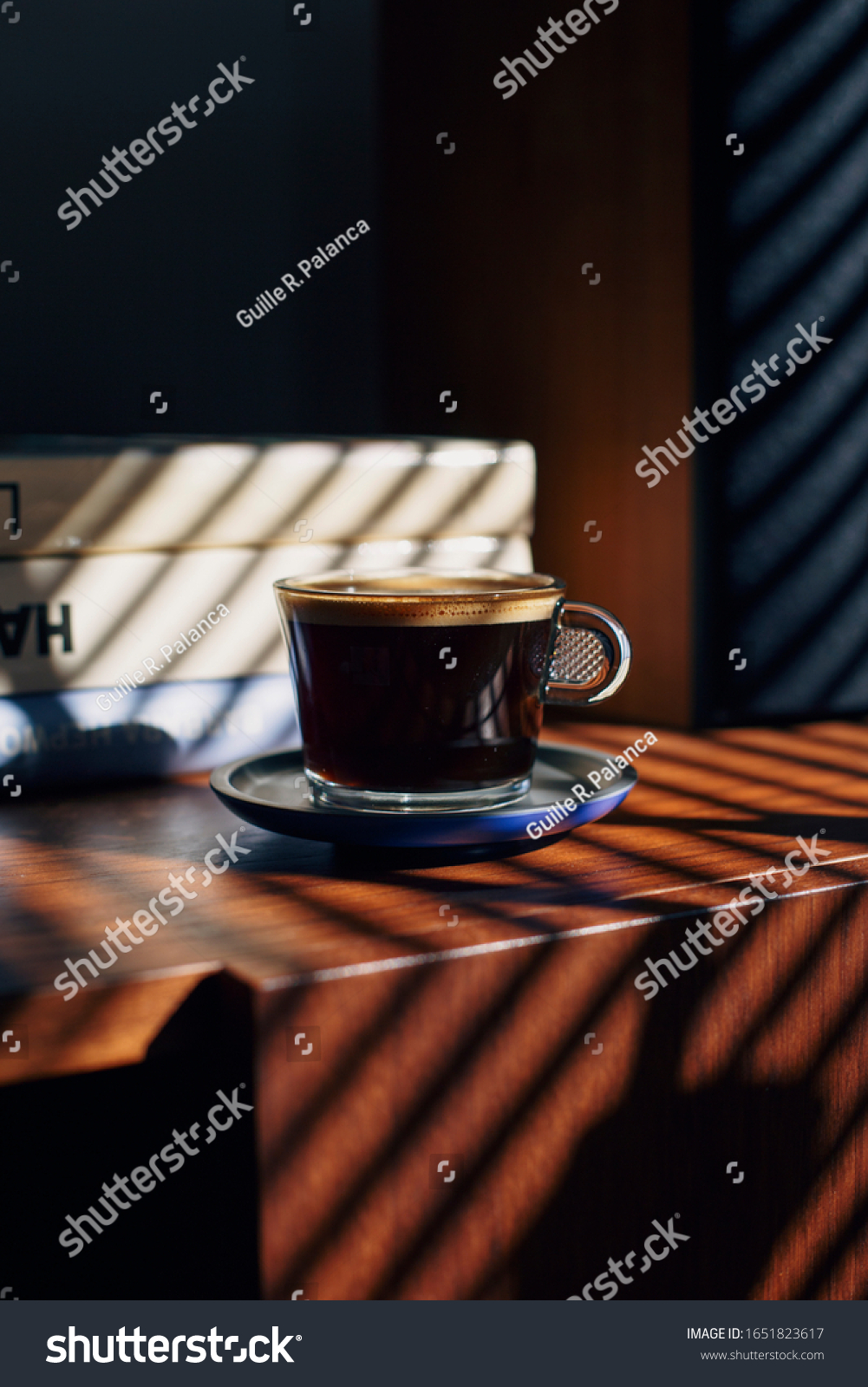 Coffee cup on a brown table with books and speaker behind. 