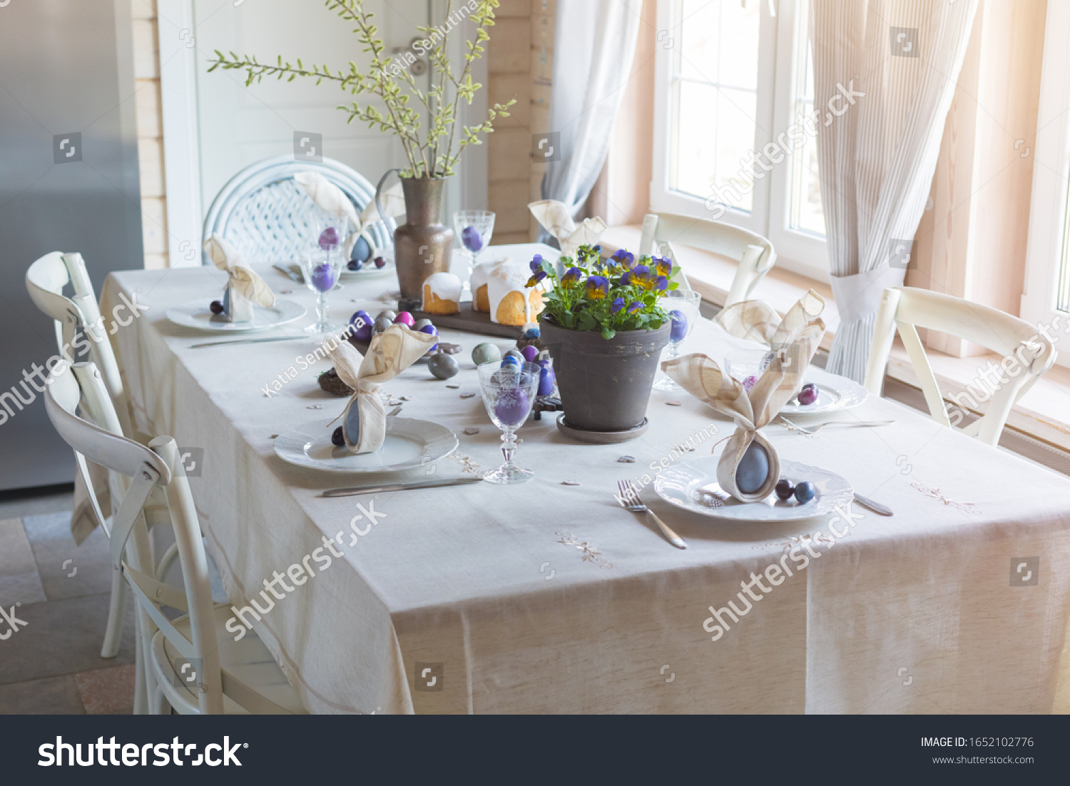 Easter festive spring table setting decoration bunny ears shaped napkins dyed hen's and quail eggs cakes violets potted feathers family dinner or breakfast concept banner