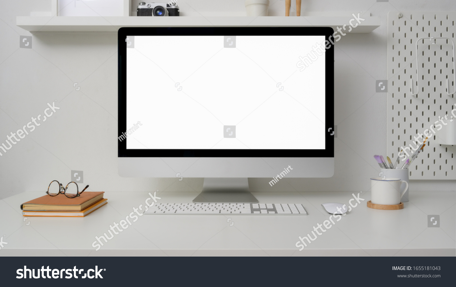 Close up view of minimal workspace with blank screen computer  office supplies and decorations on white desk with shelf on white wall 
