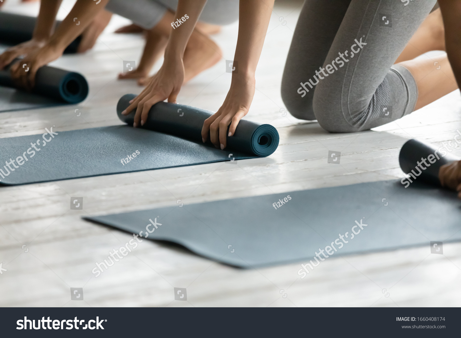 Sporty women barefoot kneeling on warm floor fold up personal mats finished yoga session at studio close up. Training class like-minded females  healthy body and mind  lifestyle and wellness concept