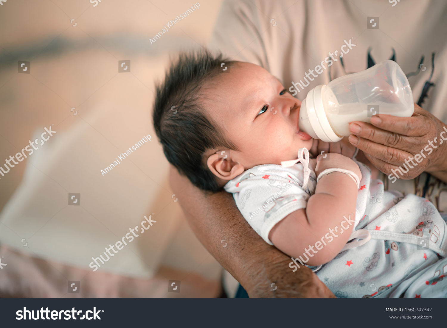 Baby is drinking milk from a bottle hold by the mother.