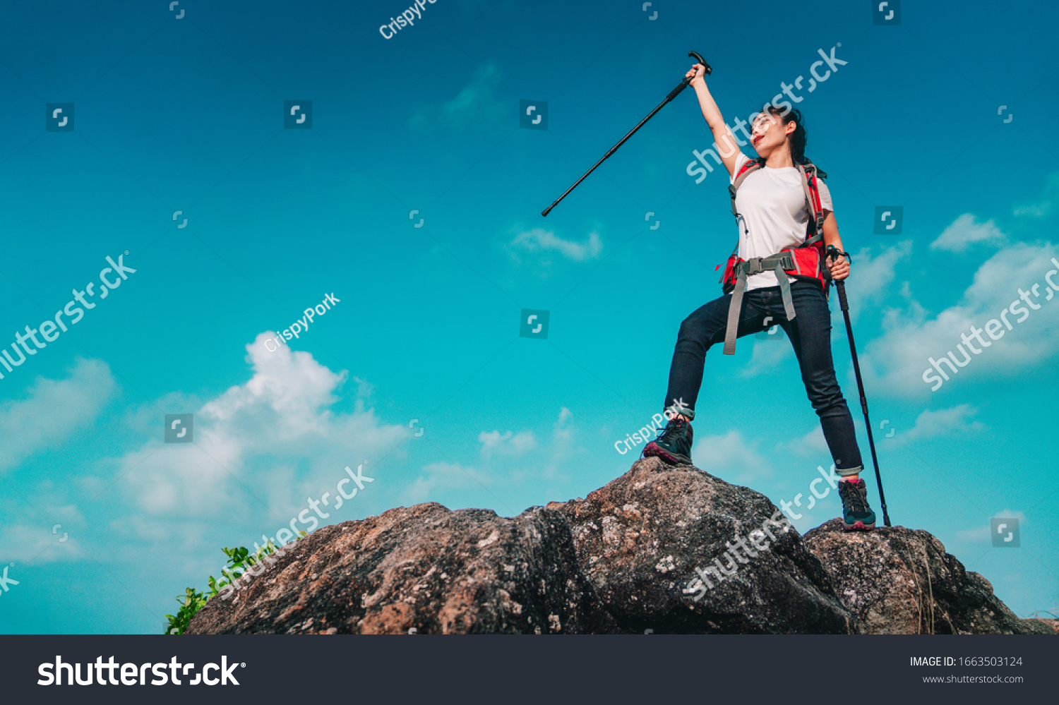 Young asian women hikers climbing up on the peak of mountain near ocean. Woman hiking in the mountains standing on a rocky summit ridge with backpack and pole looking out over ocean landscape