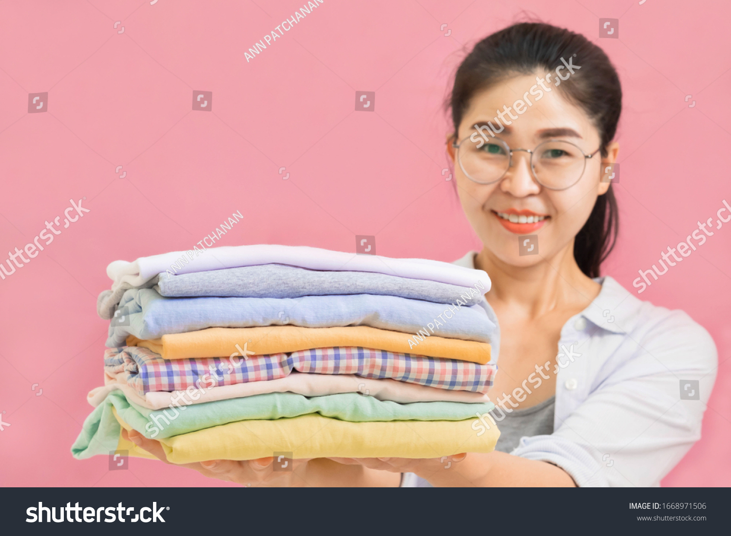 Young beautiful asian Woman holding Stacks of folded washed and dried clothes pile on pink wall background Selective focus