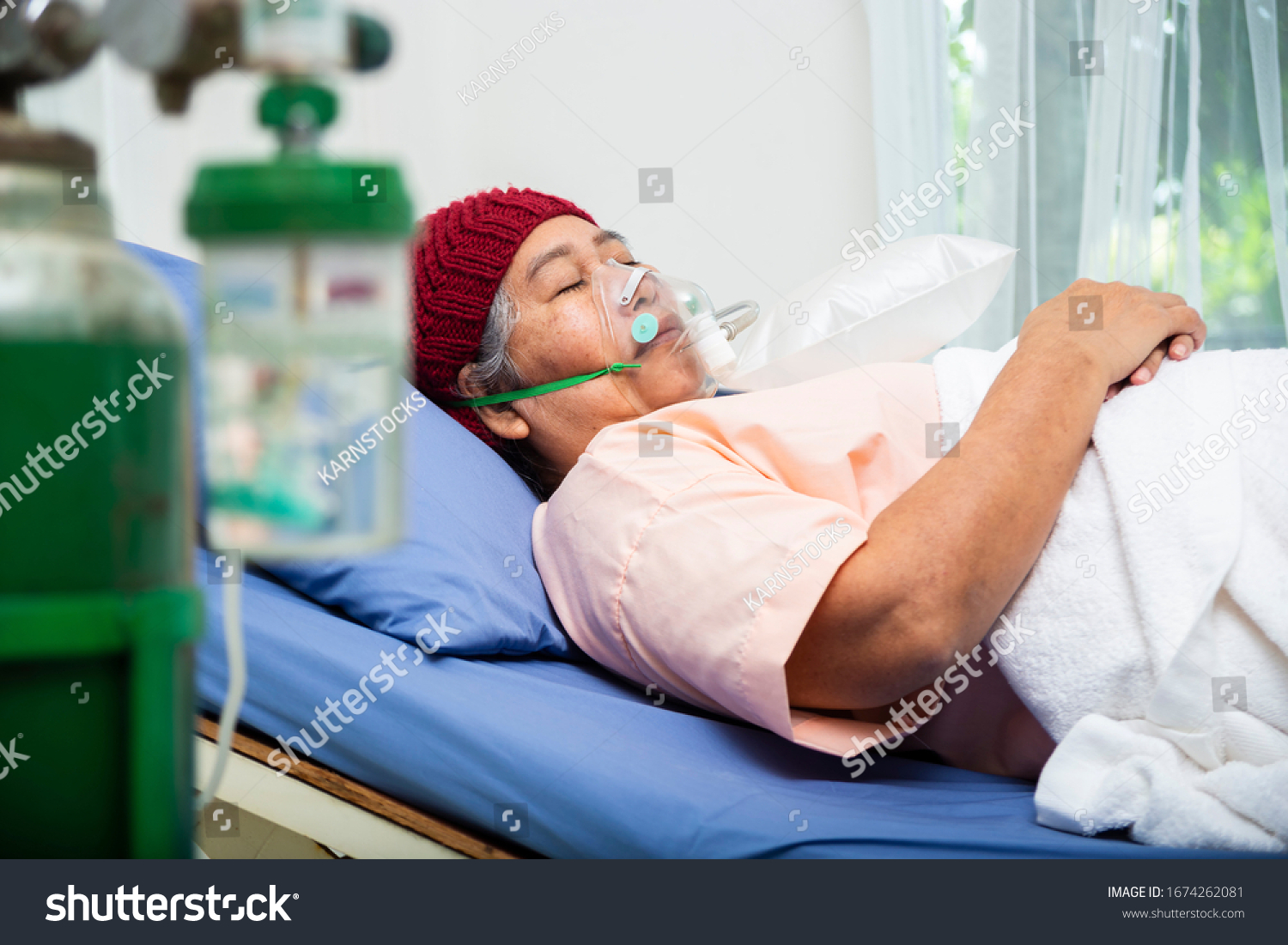 Asian elderly woman wearing wool hat with oxygen mask to breathing while lying on patient bed senior female medical and healthcare concept