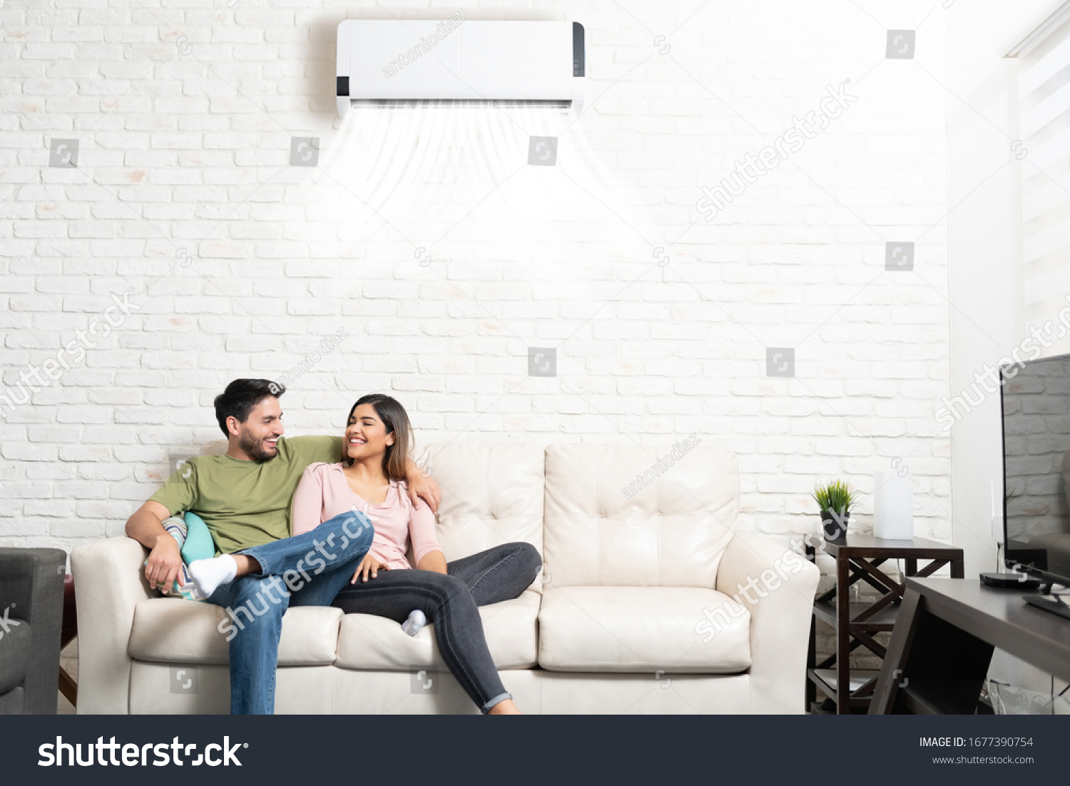 Happy Latin boyfriend and girlfriend relaxing on sofa in living room at home with air conditioning
