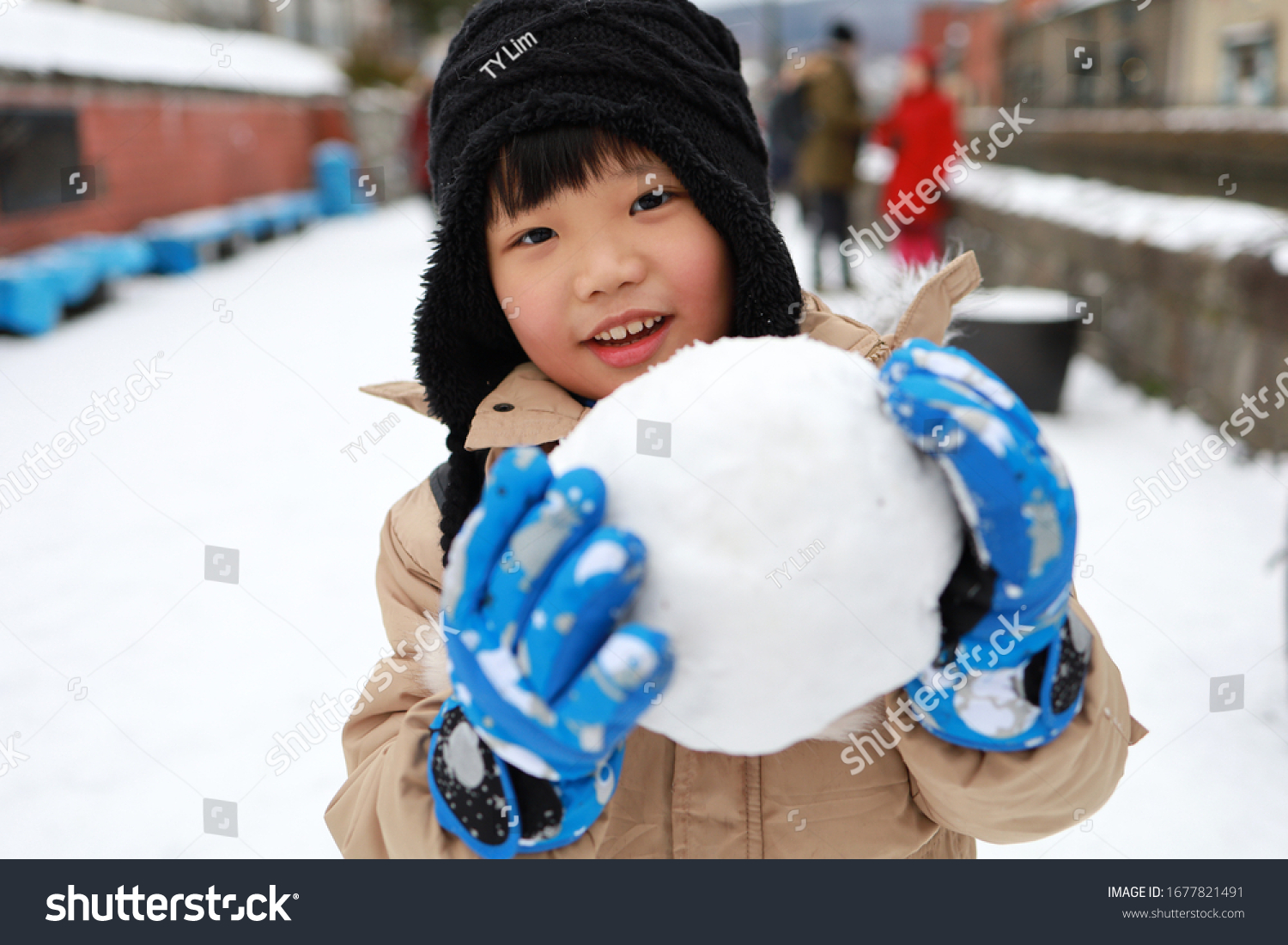 Cute Asian child playing on snow in the park.