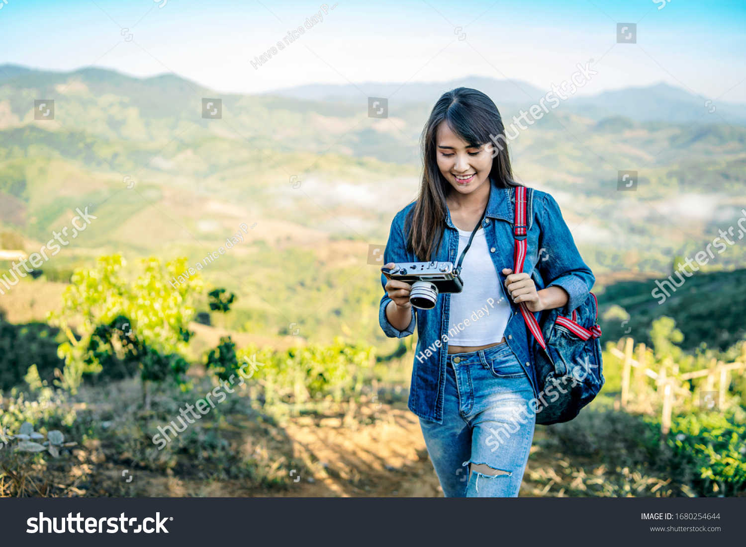 asian tourist traveler girl in an adventure traveling on the mountains using a digital camera taking a photograph of the misty mountain view in the morning sunrise wearing a denon jacket and backpack
