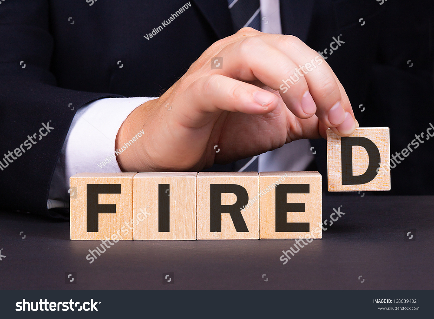 An American businessman is building the word Fired from wooden building blocks. Business concept.