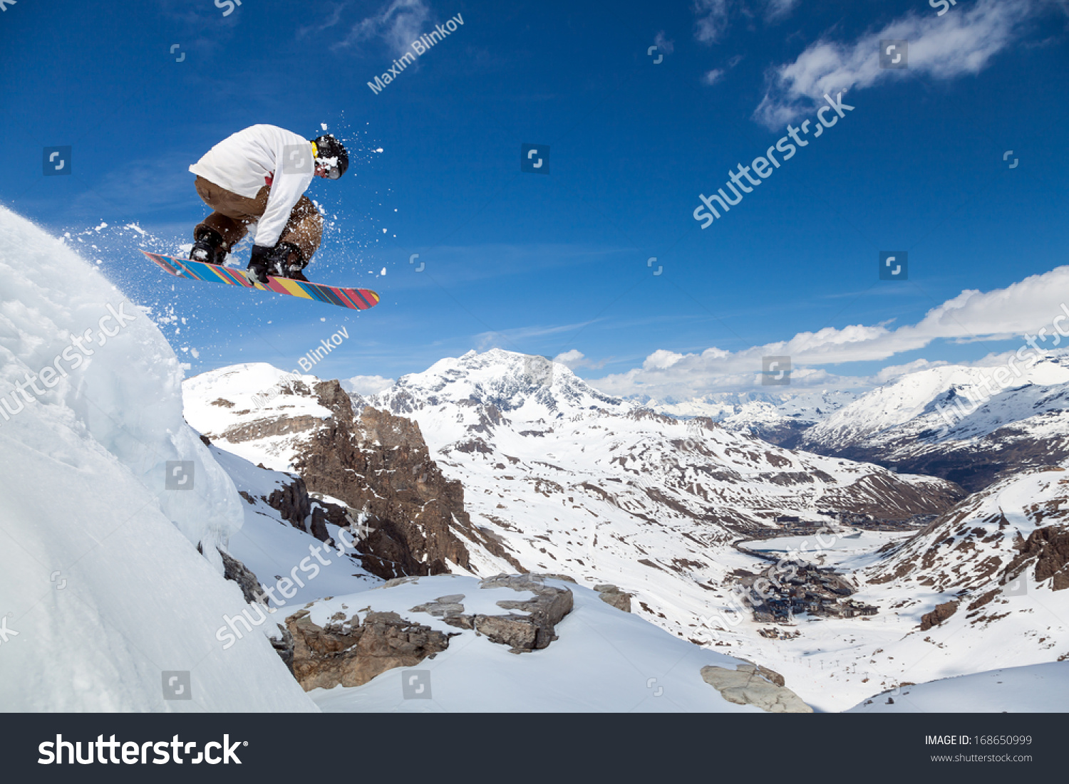 Jumping snowboarder keeps one hand on the snowboard on blue sky background