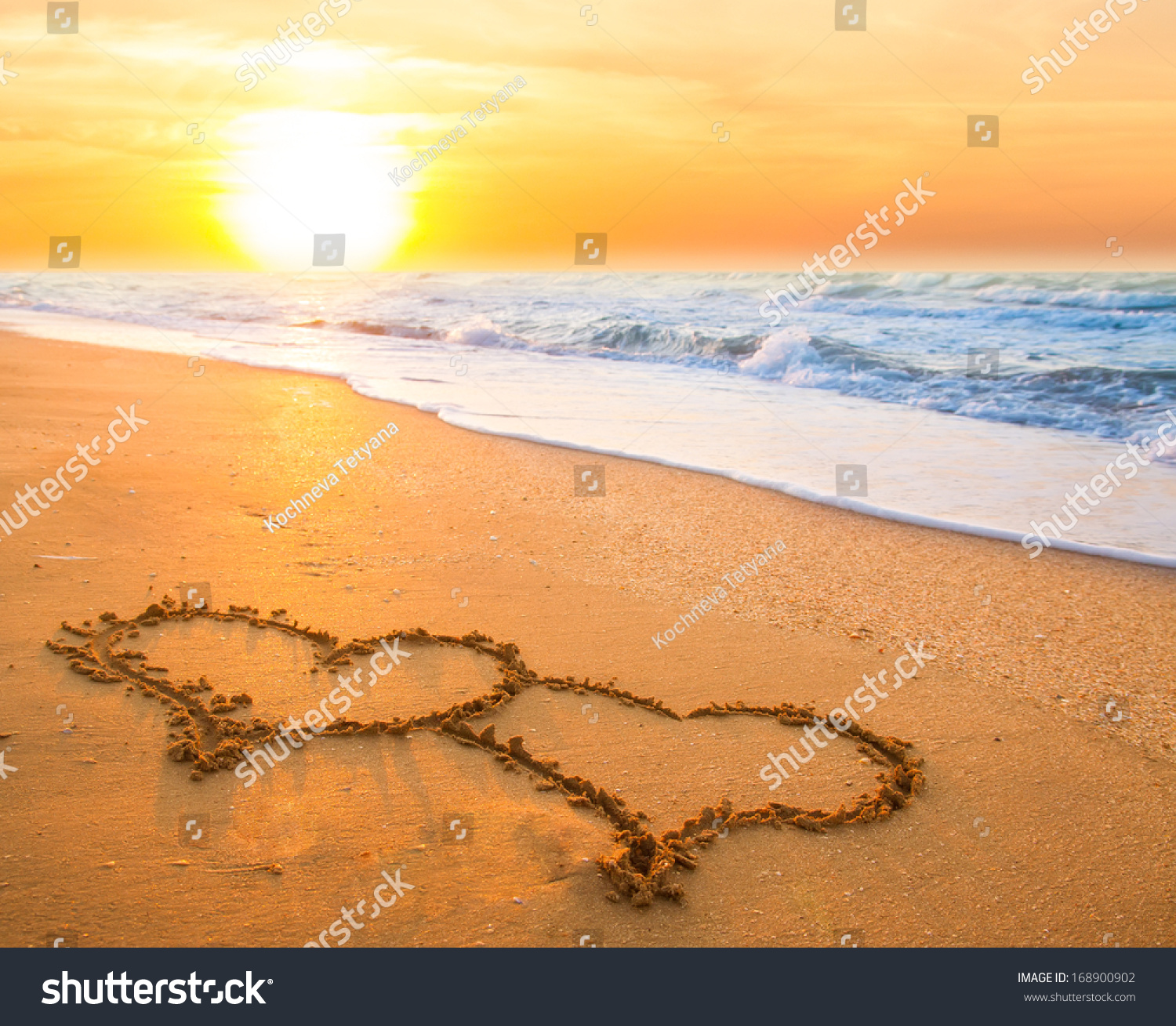 two hand drawn hearts on beach sand over sunset