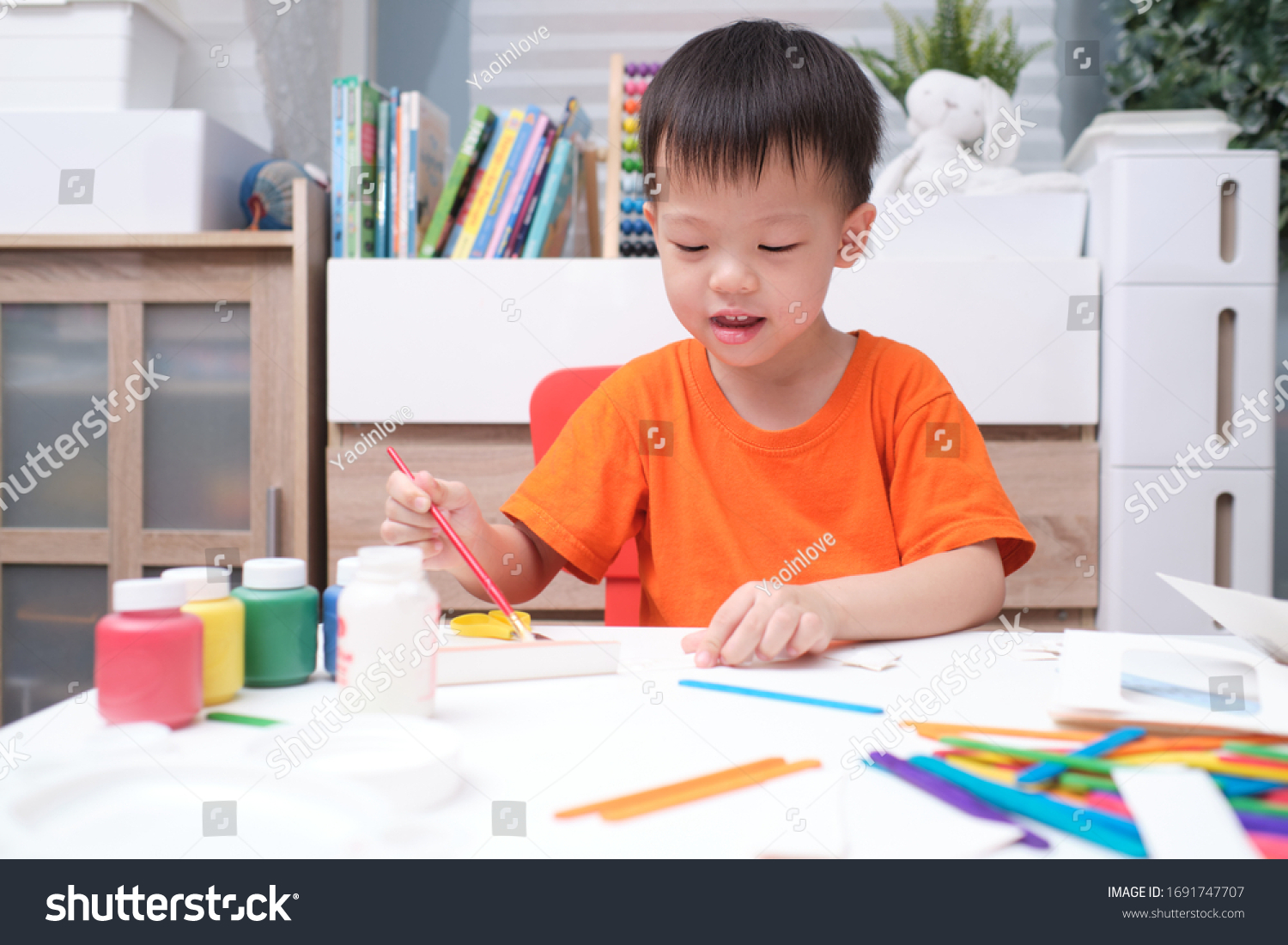 Cute happy smiling little Asian 3 years old toddler boy enjoy using glue doing arts at home  Fun paper and glue crafts for toddlers  Children's Art Project  DIY Toys for kids concept