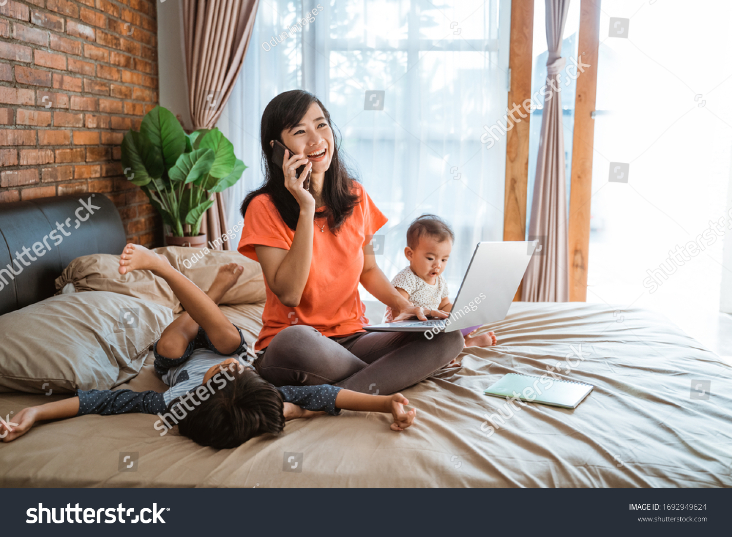 asian young woman working while taking care of her children at home