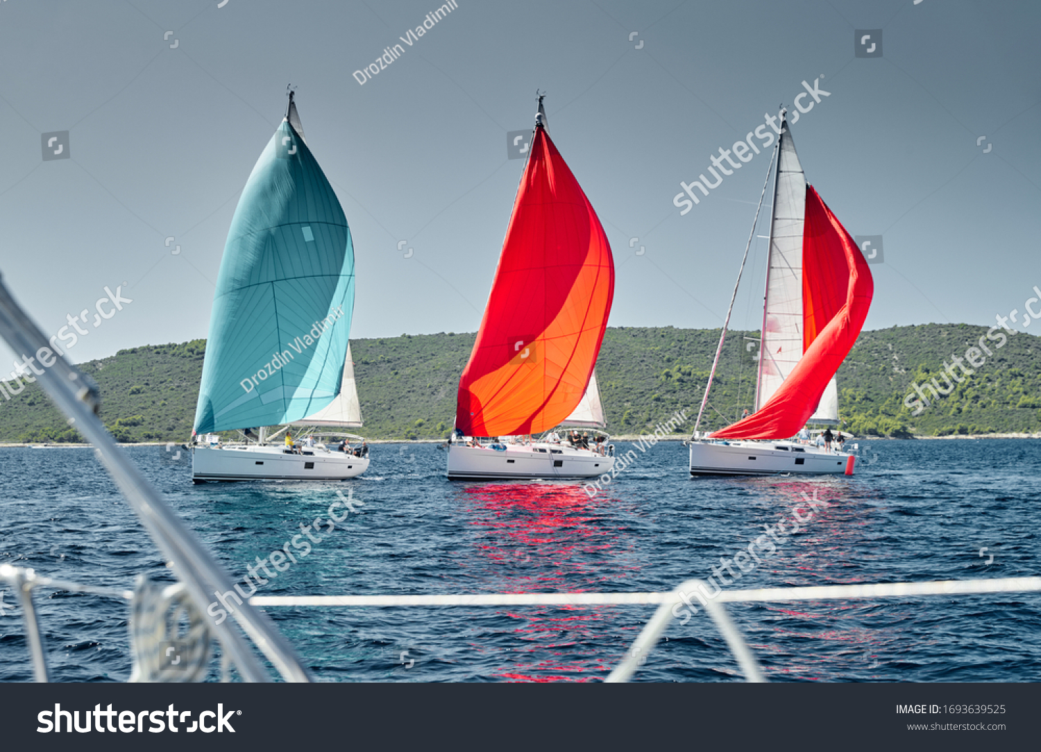 Sailboats compete in a sail regatta at sunset view throug the ropes race of sailboats reflection of sails on water multicolored spinnakers island is on background clear weather