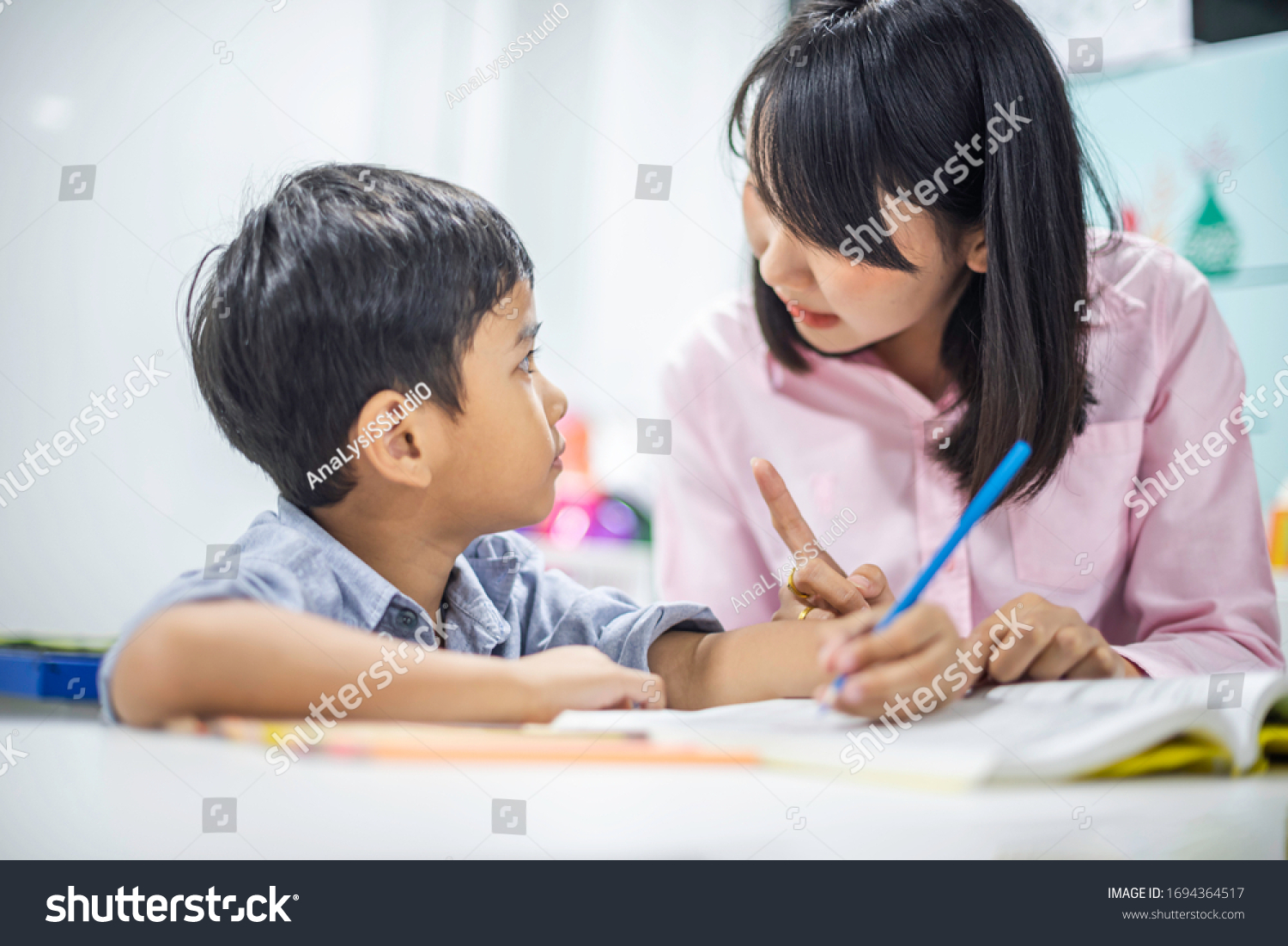 Asian female teacher teaching kid writing lesson and reading book in classroom pecial education during school holidays.