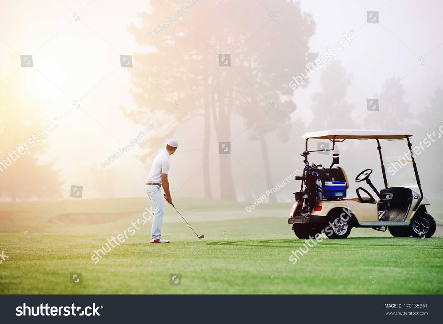 Golfer lining up shot with iron club on golf course in fairway at sunrise