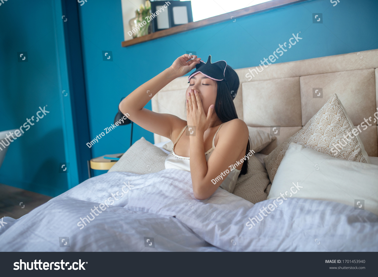 AAt home. Young woman in sleeping eye mask yawning in bed