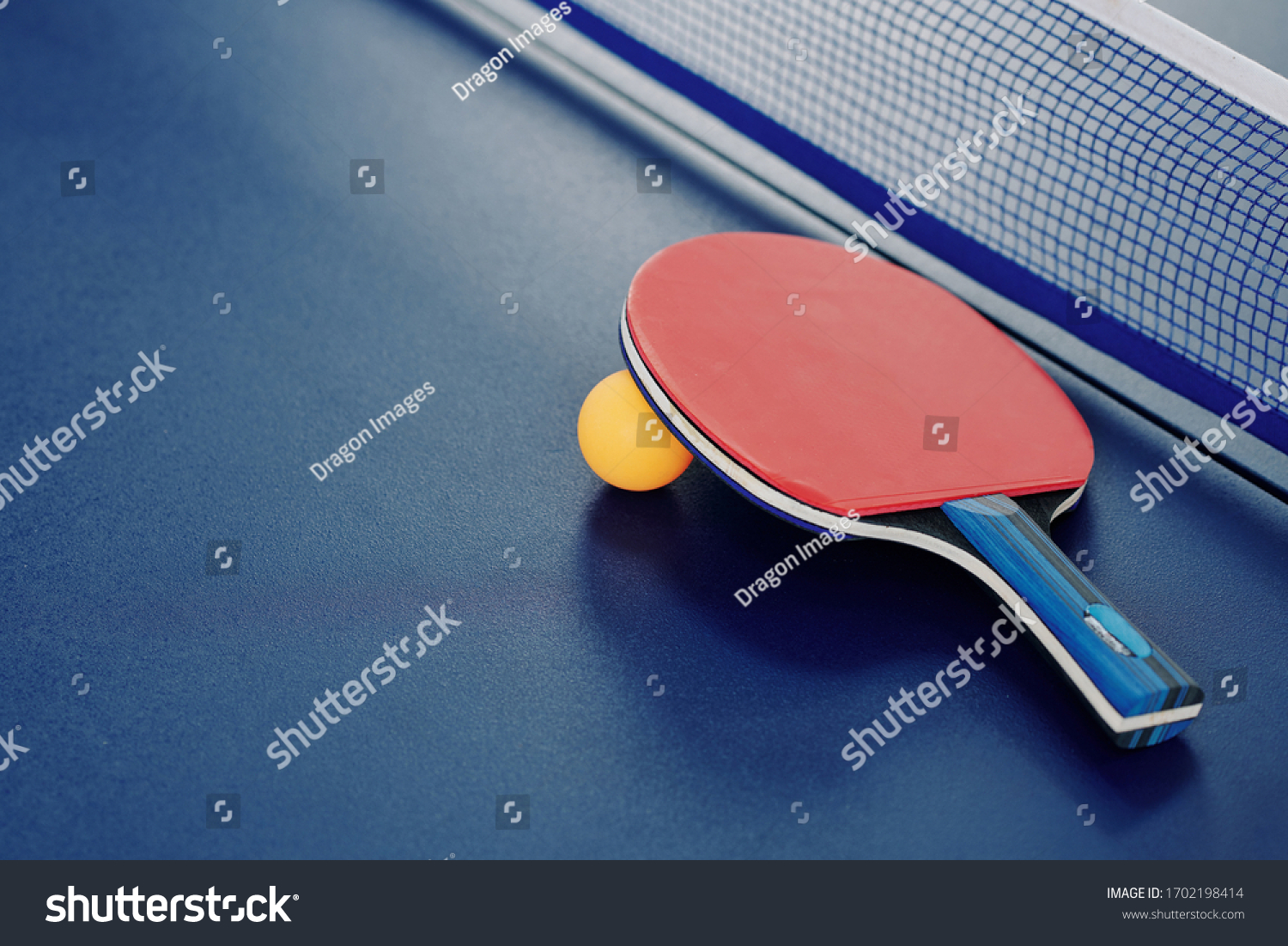 Close-up image of ping-pong racket and orange ball ion table with net