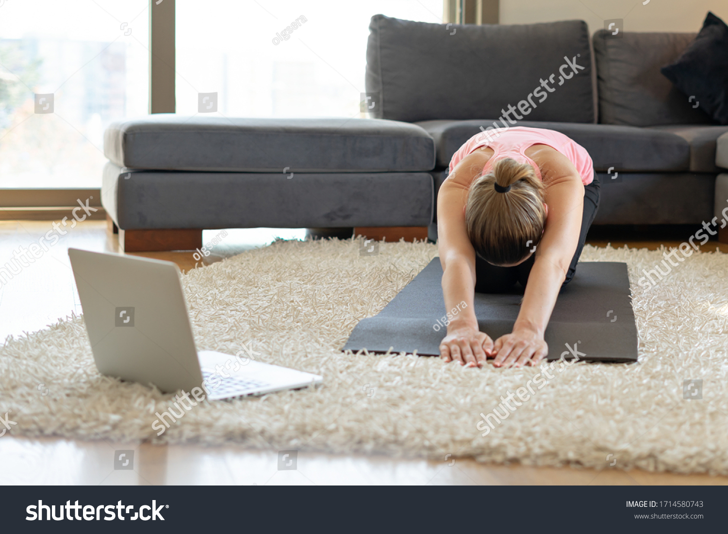 young woman and doing exercises on yoga mat opposite laptop