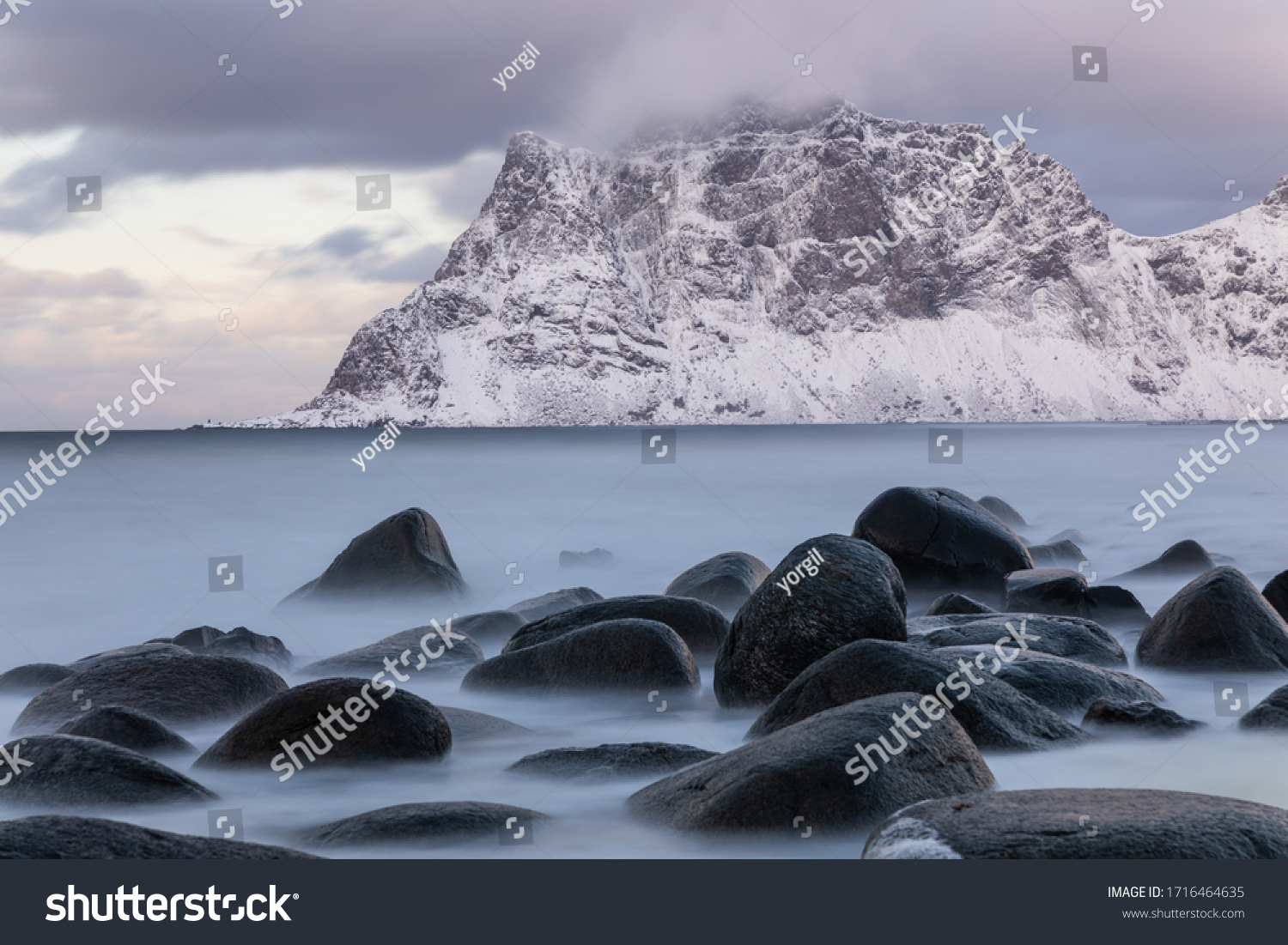 Long exposure capture of Uttakleiv beach Lofoten Norway. Soft sea and rocks. Snow covered mountain in background. Calm winter scene.