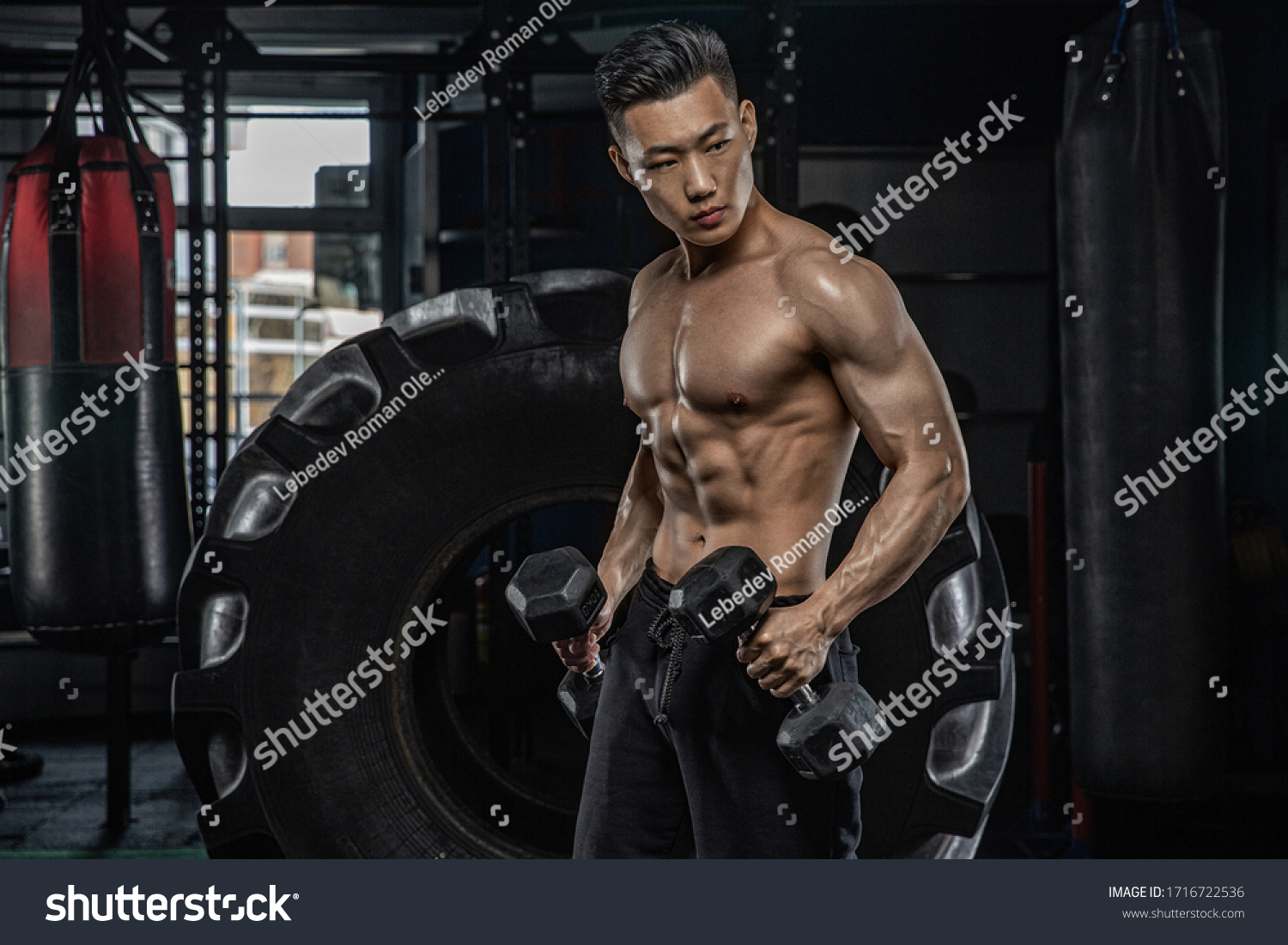 Asian handsome man posting with dumbbells in dark gym