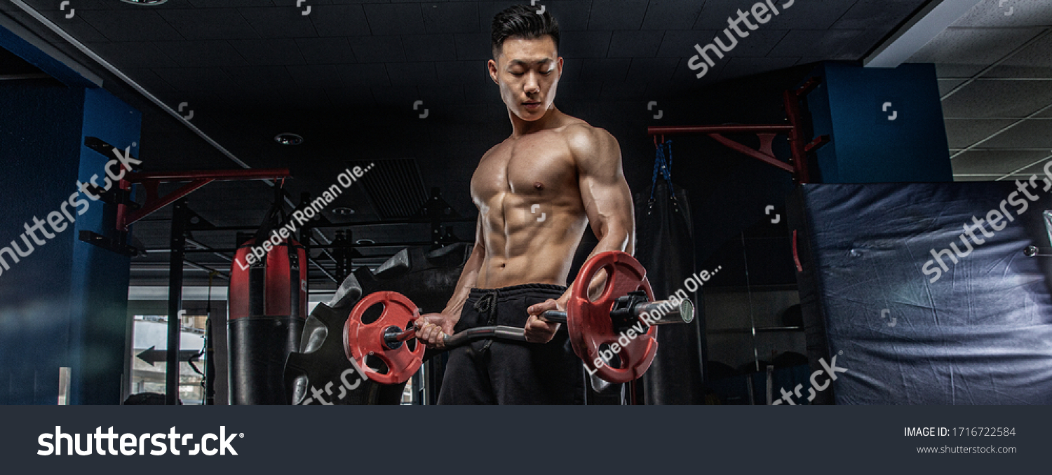 Asian handsome man posting with dumbbells in dark gym