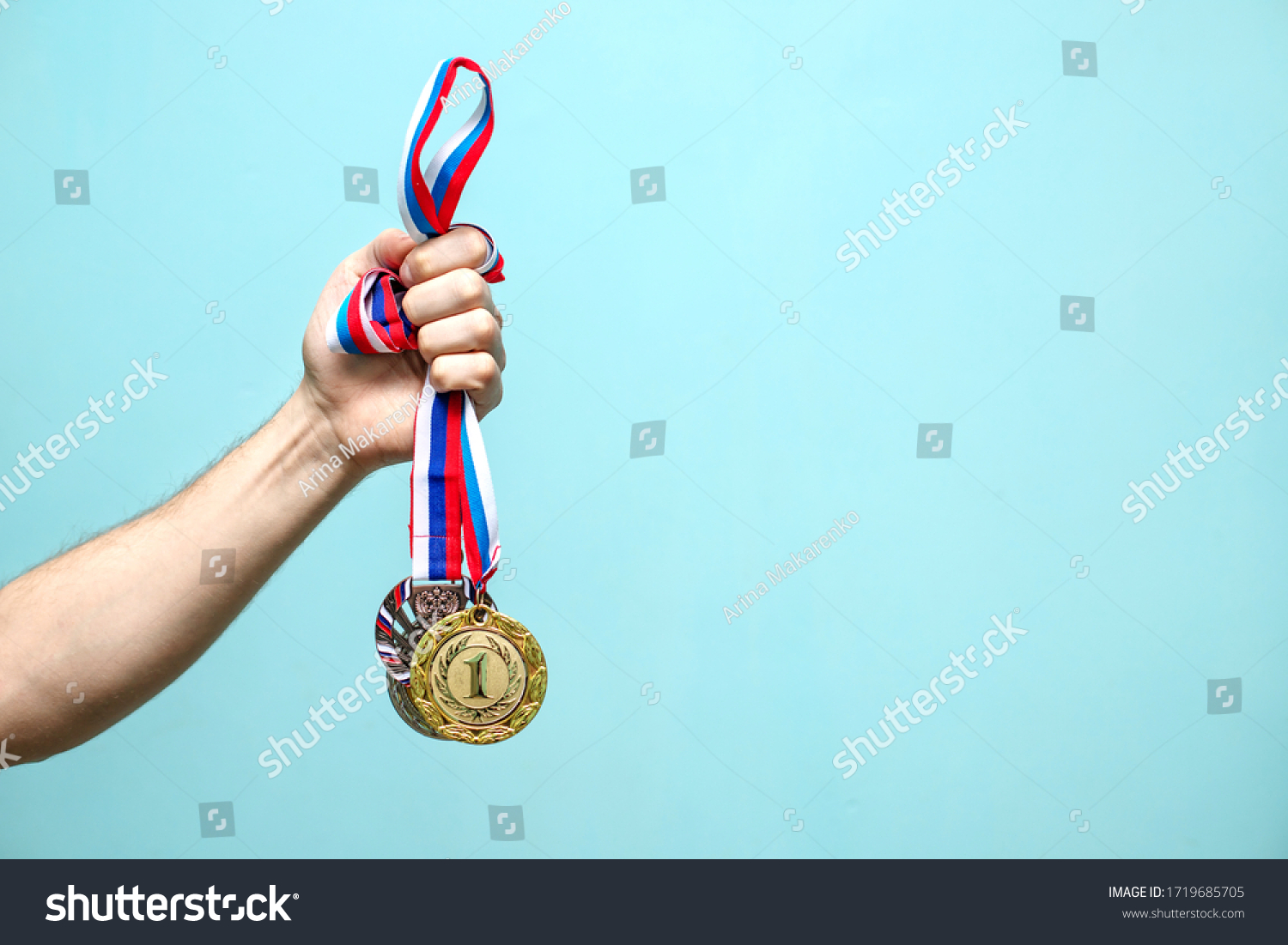 the male hand of the winning athlete holds the highest-ranking medals on a blue background space for text