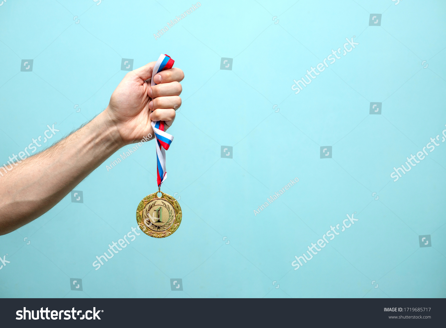 the male hand of the winning athlete holds the gold medal on a blue background space for text