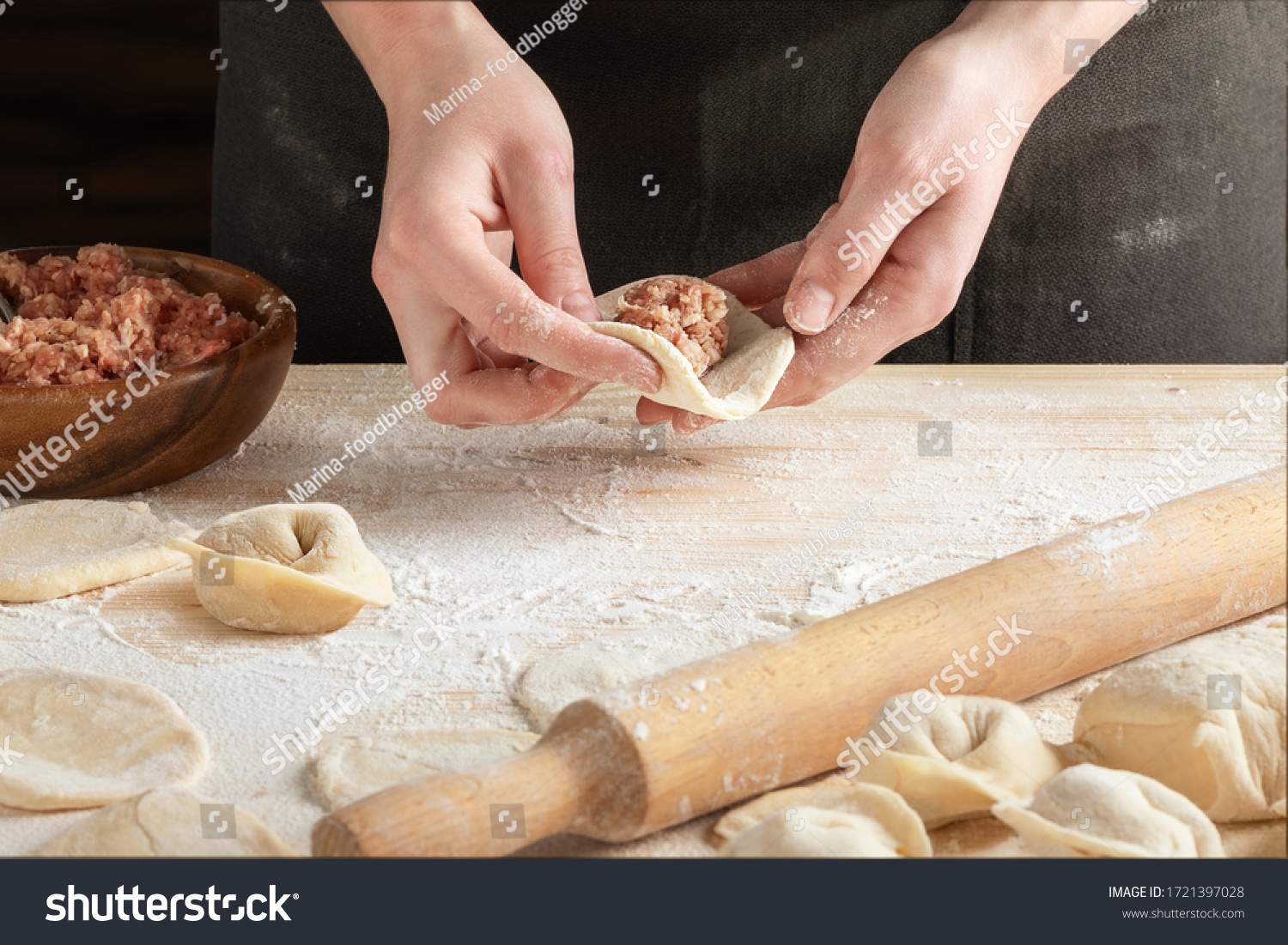 Front view of woman's hands making meat dumpling with wooden rolling pin. 