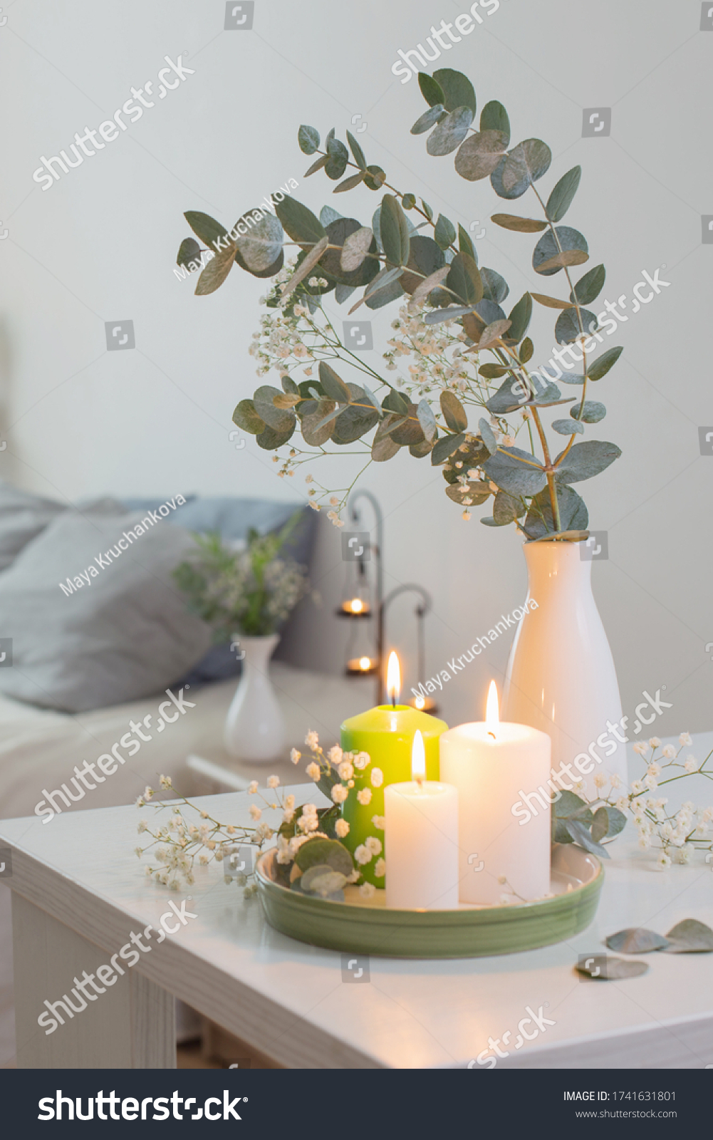 burning candles and eucalyptus in  vase in white bedroom