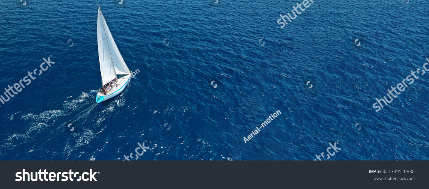 Aerial drone ultra wide photo of beautiful sail boat with white sails sailing open ocean deep blue sea