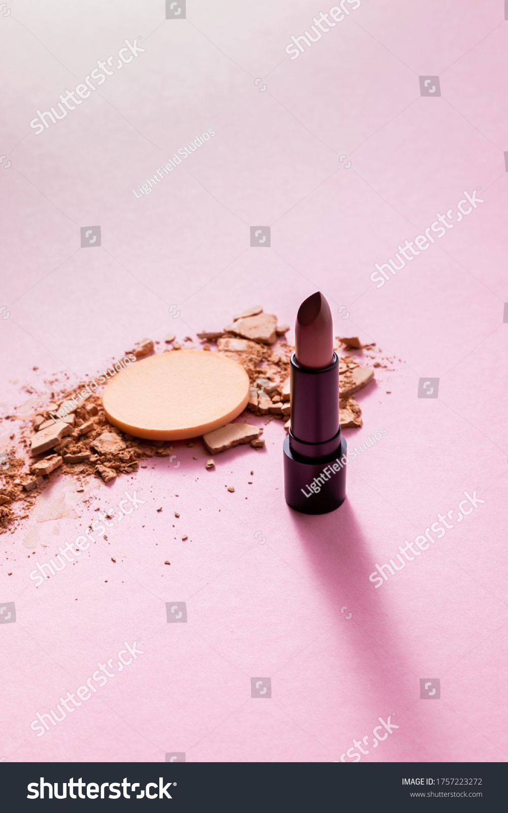 cracked face powder near makeup sponge and lipstick on pink
