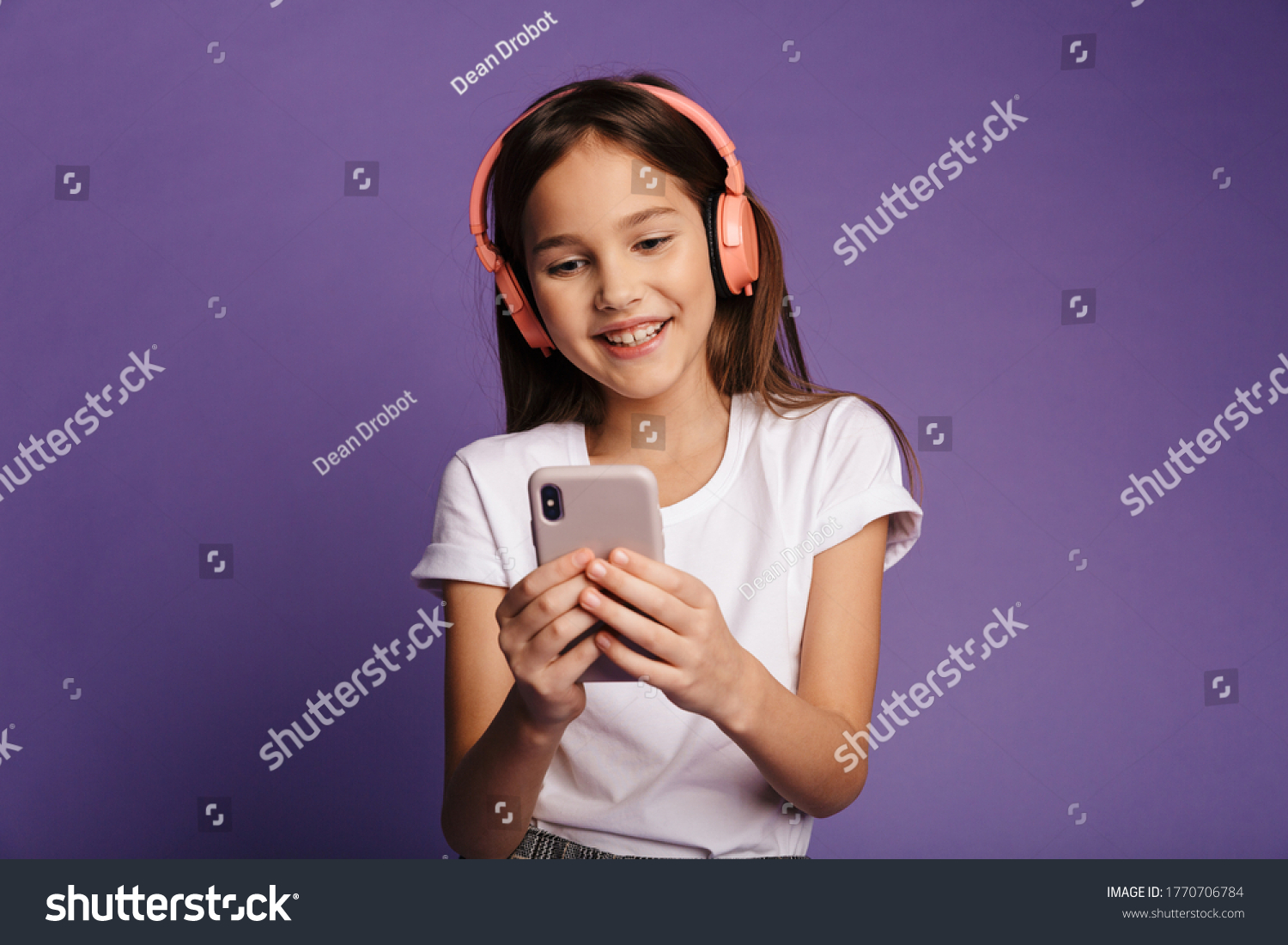 Photo of laughing attractive girl using wireless headphones and mobile phone isolated over purple background