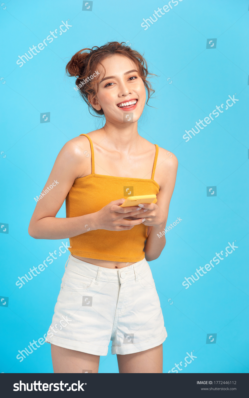 pretty smiling girl in summer clothes using mobile phone while standing 
