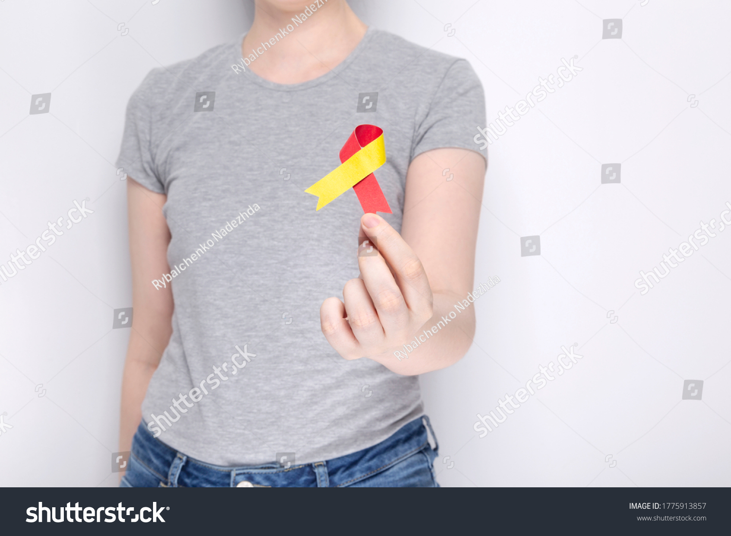 World Hepatitis Day concept. Girl in gray T-shirt holds in her hand awareness symbol red-yellow ribbon. Gray background. Copy space