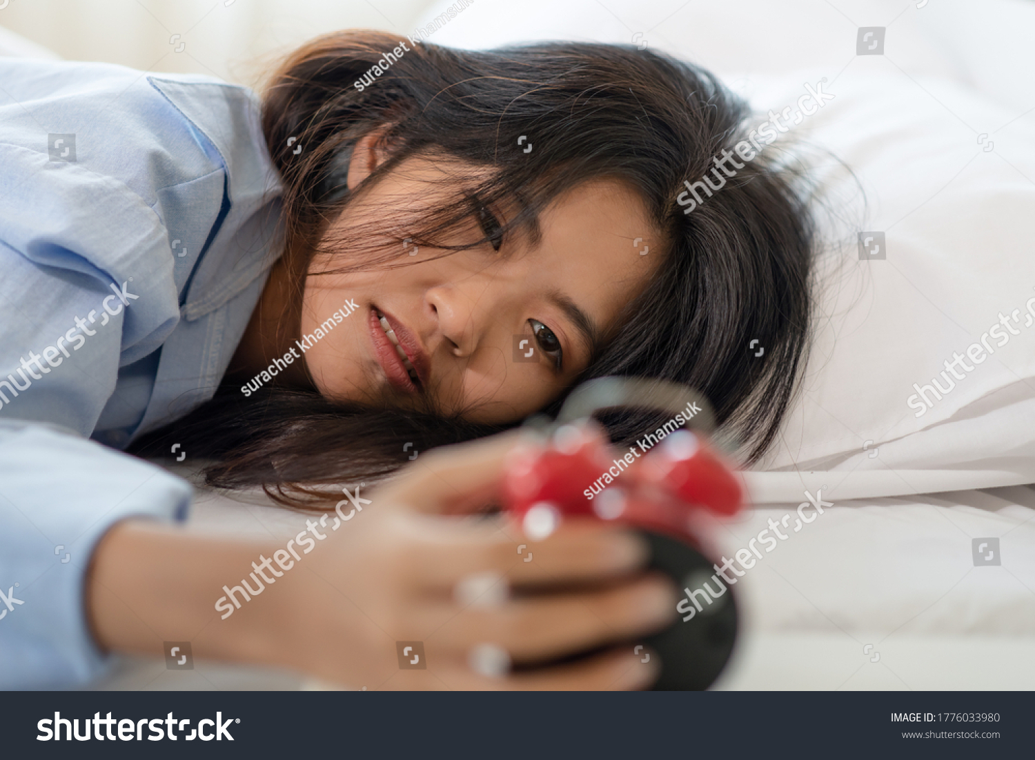 Young Asian woman laying on bed and watching her alarm clock in the morning