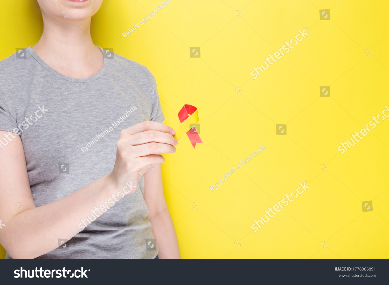 World Hepatitis Day concept. Girl in gray T-shirt holds in her hand awareness symbol red-yellow ribbon. Yellow background. Copy space
