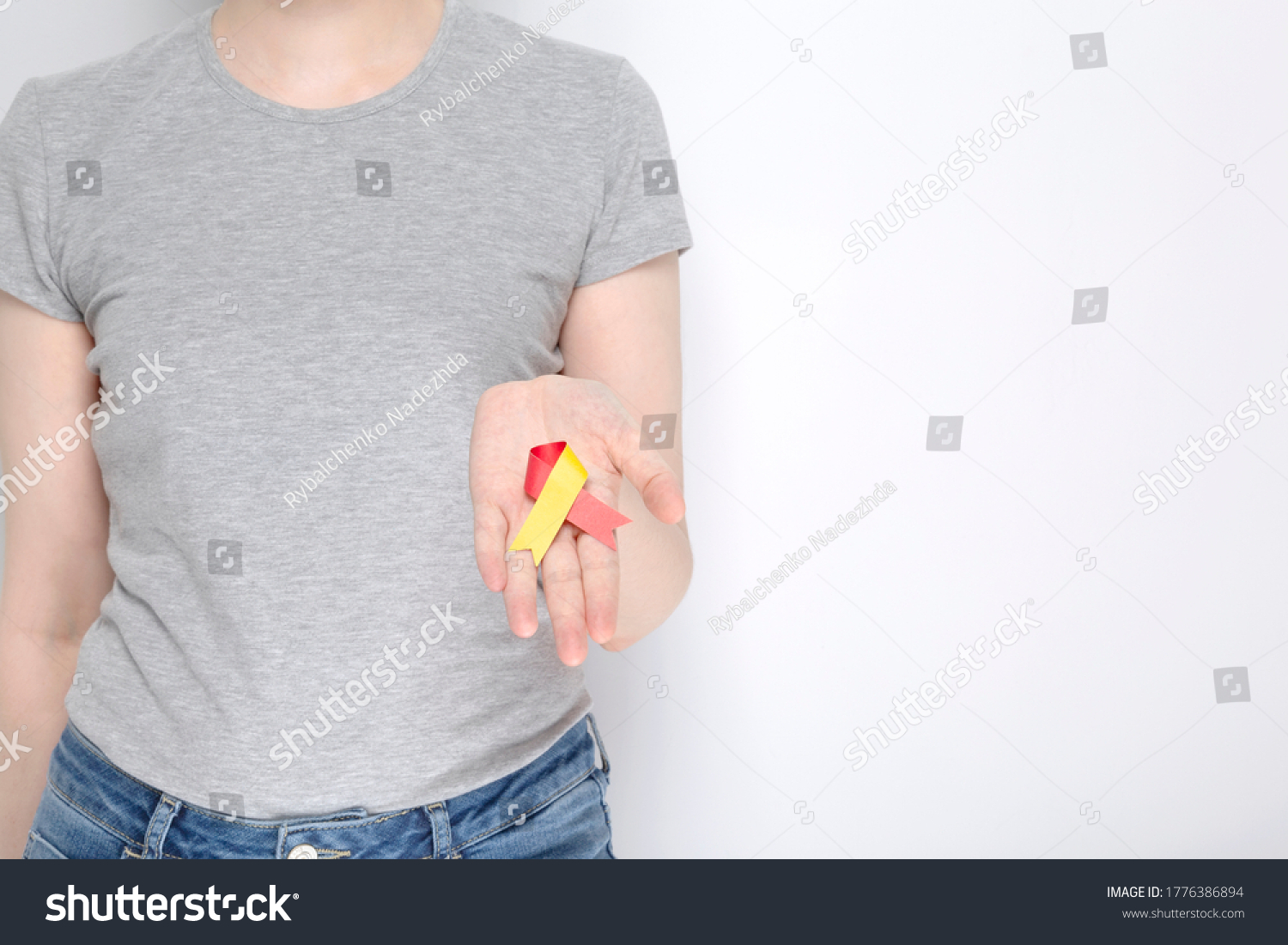 World Hepatitis Day concept. Girl in gray T-shirt holds in her hand awareness symbol red-yellow ribbon. Gray background. Copy space