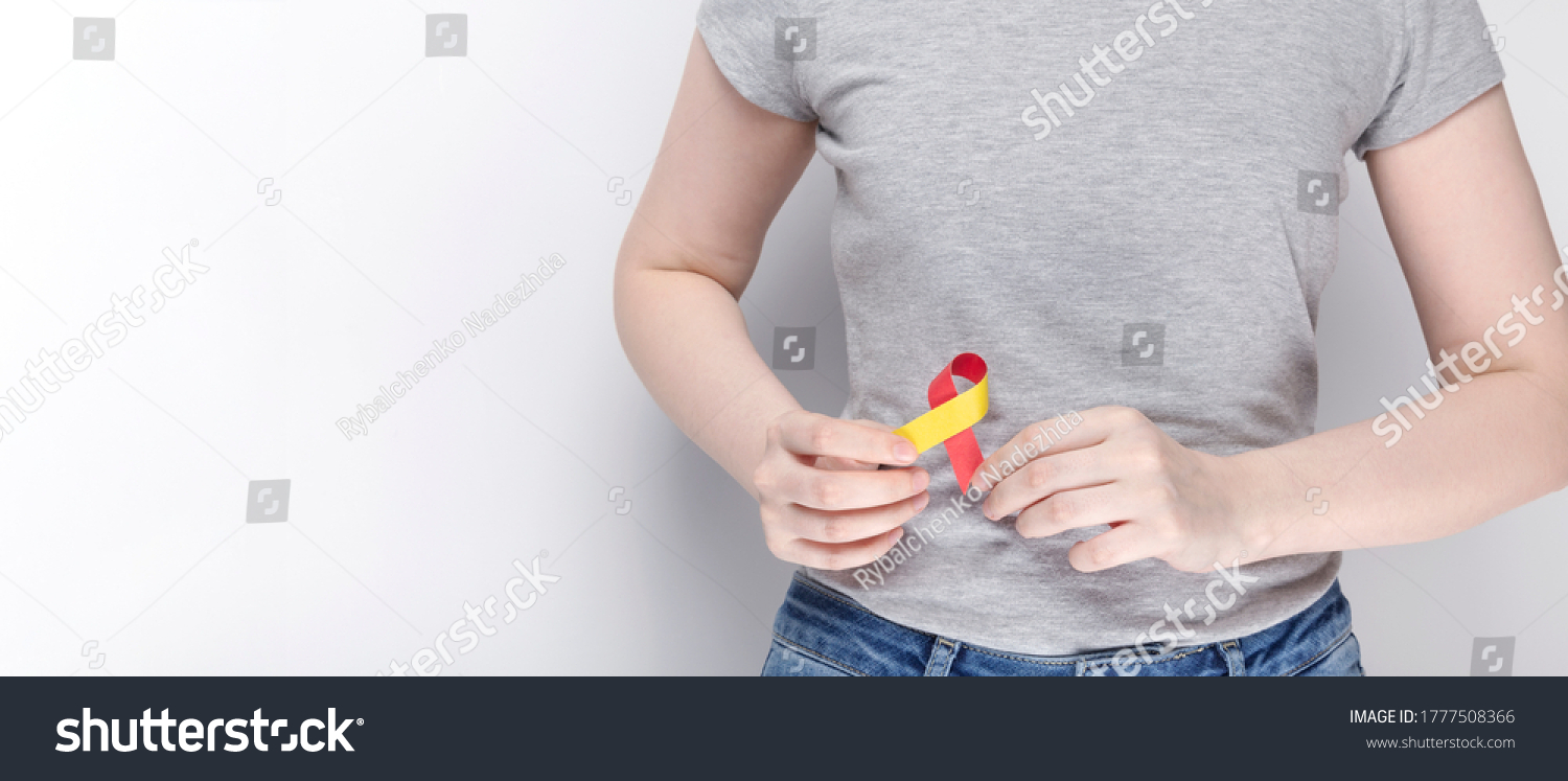 World Hepatitis Day Concept. Girl in gray T-shirt holding red-yellow ribbon area liveras symbol of awareness. Gray background. Copy space