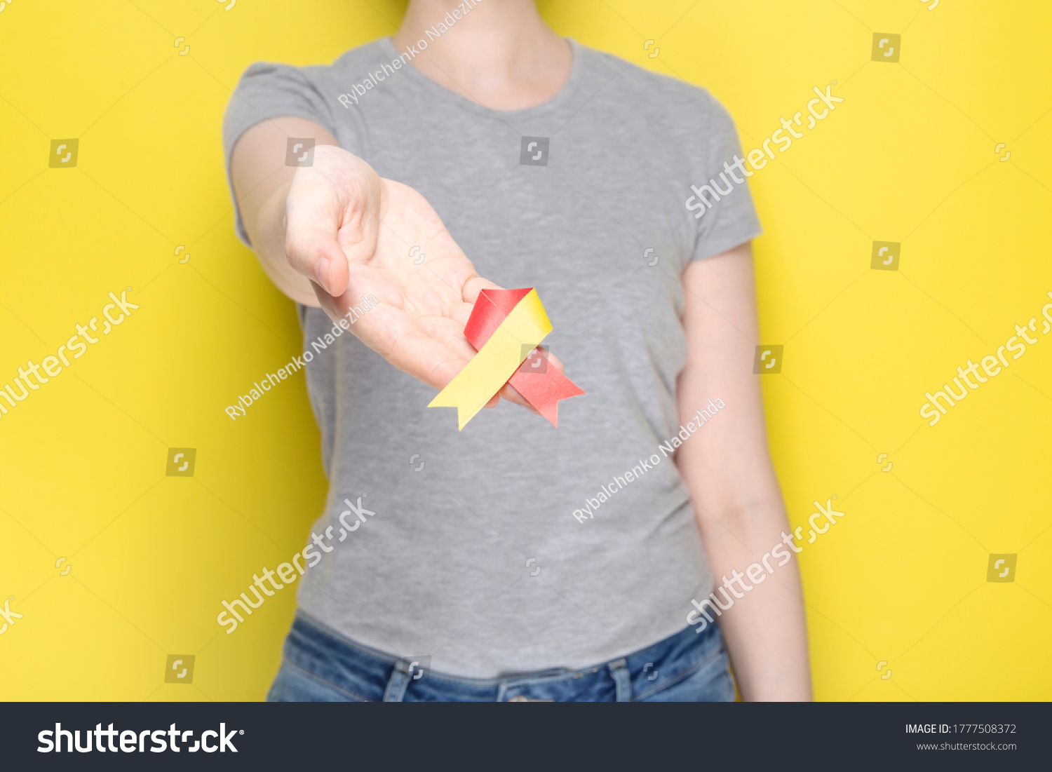 World Hepatitis Day concept. Girl in gray T-shirt holds in her hand awareness symbol red-yellow ribbon. Yellow background