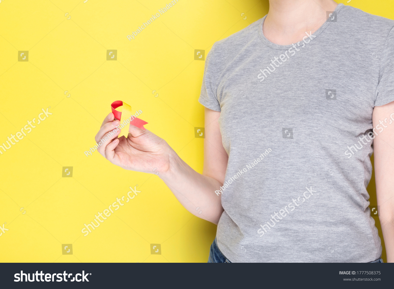 World Hepatitis Day concept. Girl in gray T-shirt holds in her hand awareness symbol red-yellow ribbon. Yellow background. Copy space