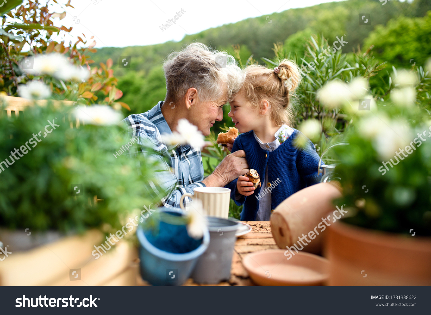 Senior grandmother with small granddaughter gardening on balcony in summer  eating.