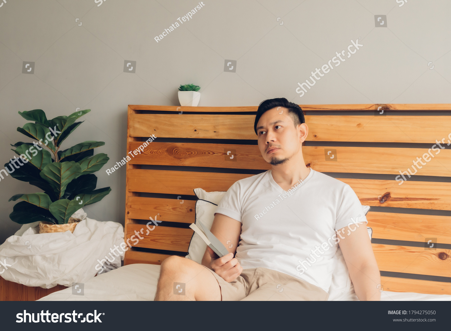 Asian man is reading book on his bed in late afternoon.