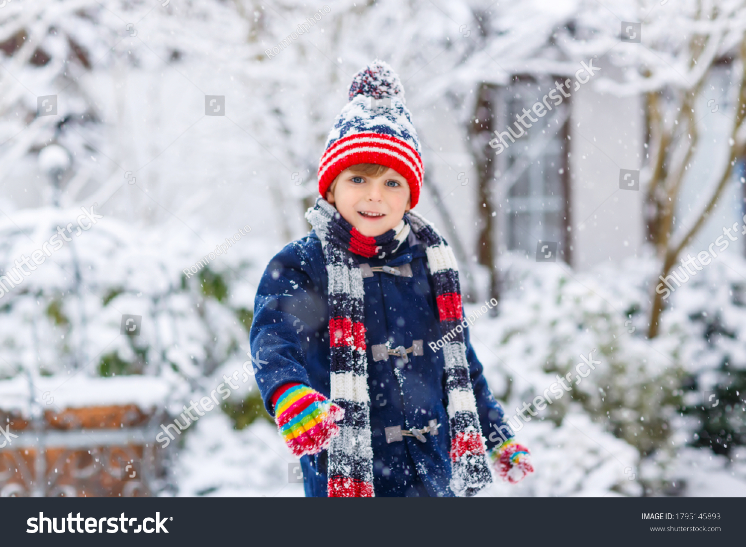 Cute little funny child in colorful winter fashion clothes having fun and playing with snow  outdoors during snowfall. Active outdoors leisure with children. Kid boy and toddler catching snowflakes.