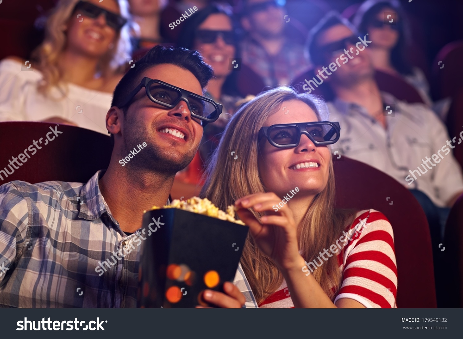 Happy couple sitting in movie theater  watching 3D movie  eating popcorn  smiling.