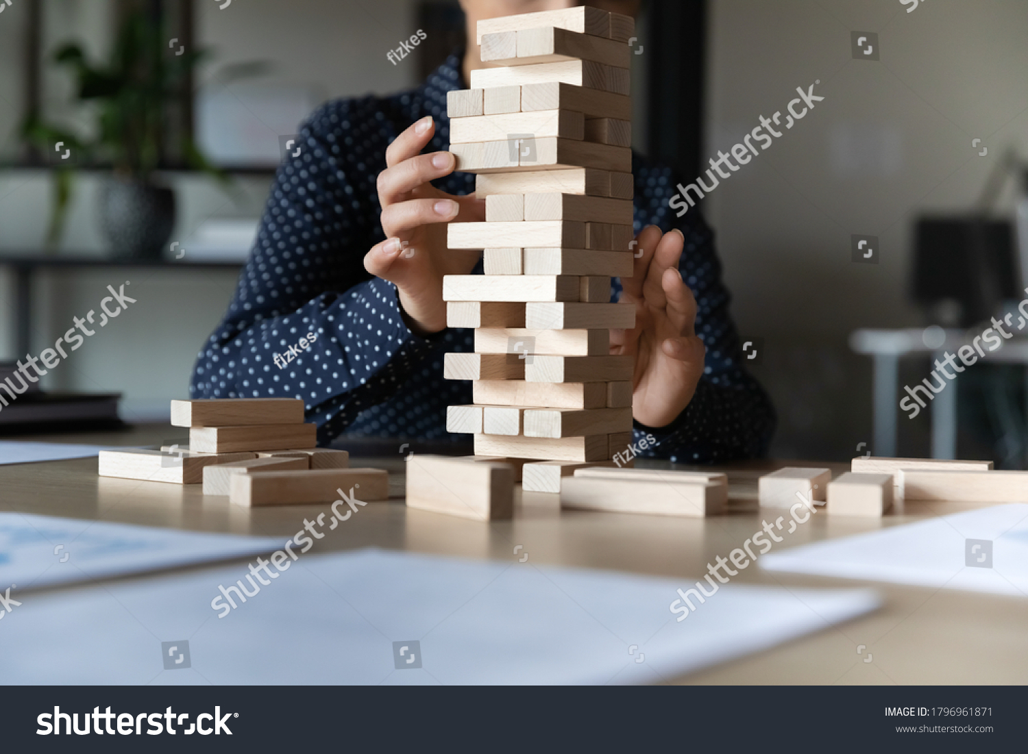 Close up young indian woman constructing tower with wooden bricks alone in office  sitting at table. Female employee manager developing strategic thinking skills or challenging at workplace.