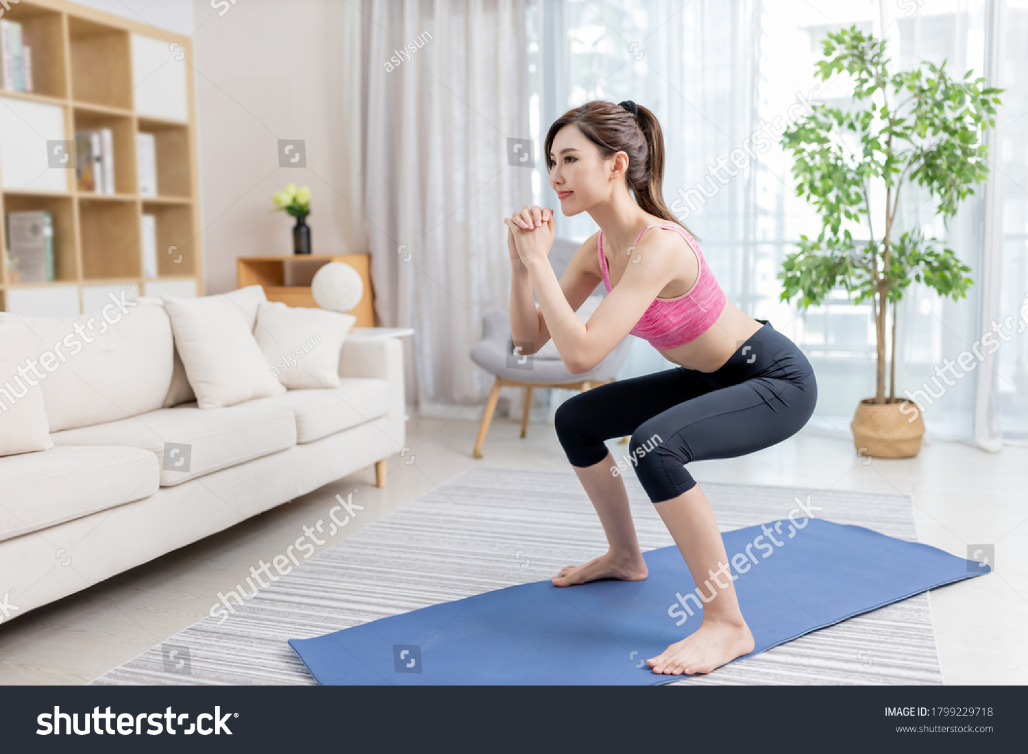 asian young woman is doing squats exercise at home